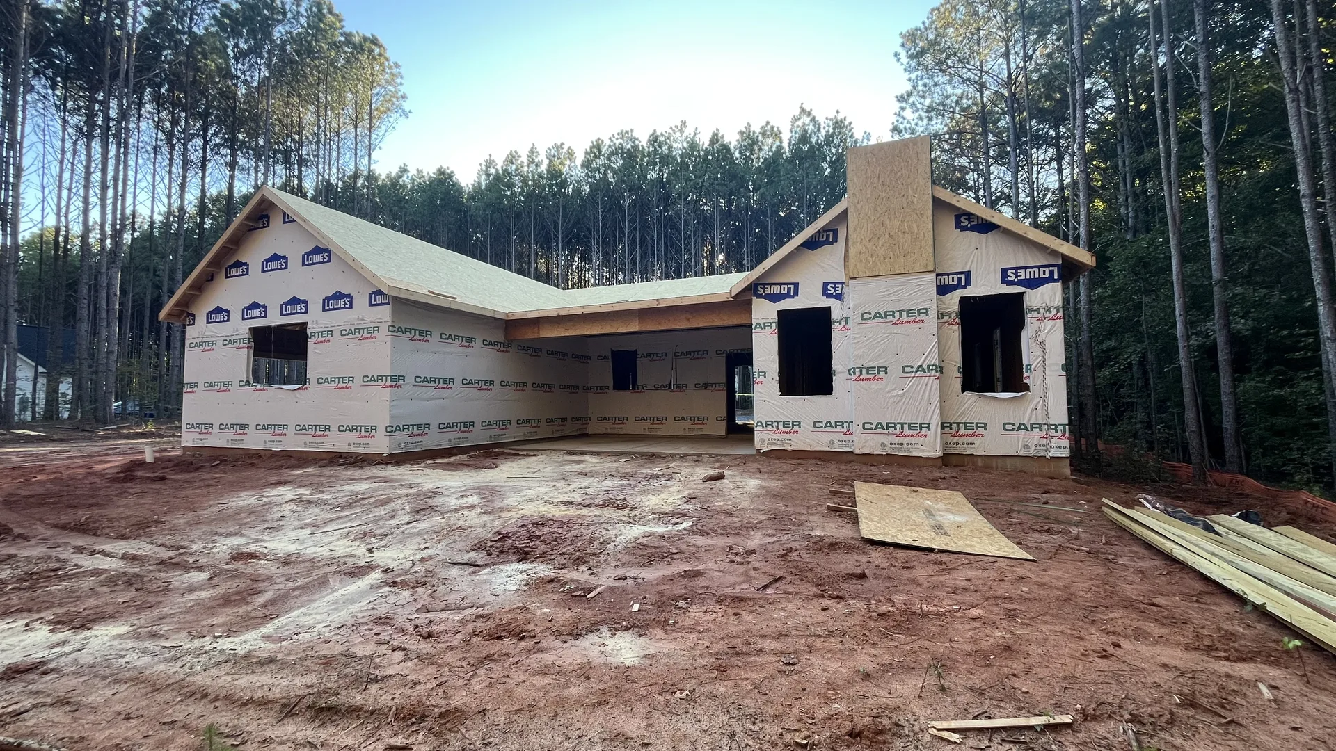 Contemporary Ranch exterior progress showing roof decking, housewrap, and window openings on the wooded York County, SC site
