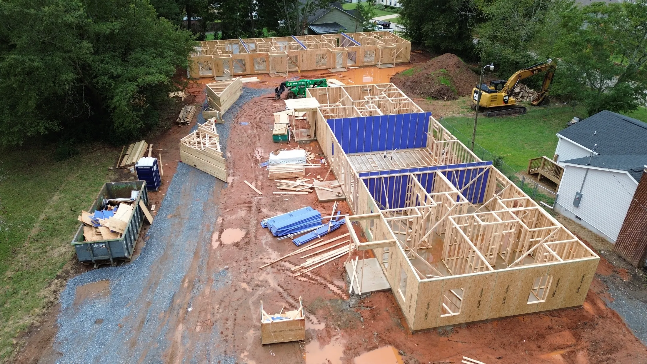 Wide drone view of the Clover, SC construction site with build-to-hold quadplex wall framing farther back